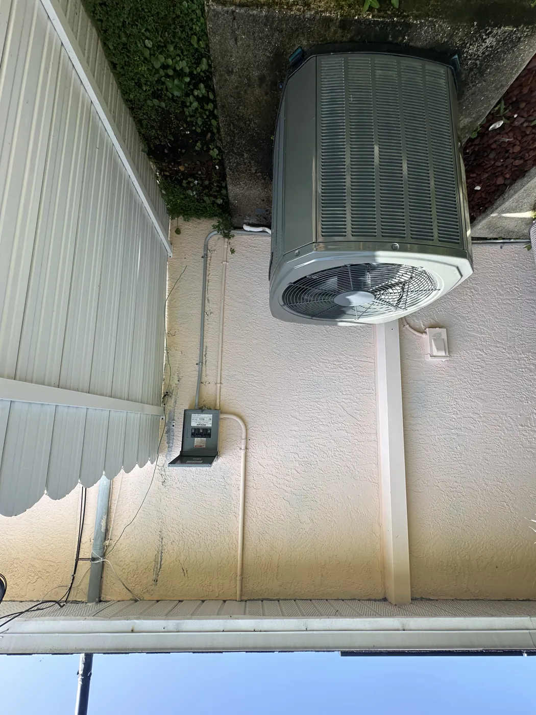 An outdoor AC condenser on a concrete pad in a narrow strip between a house wall and a wooden fence