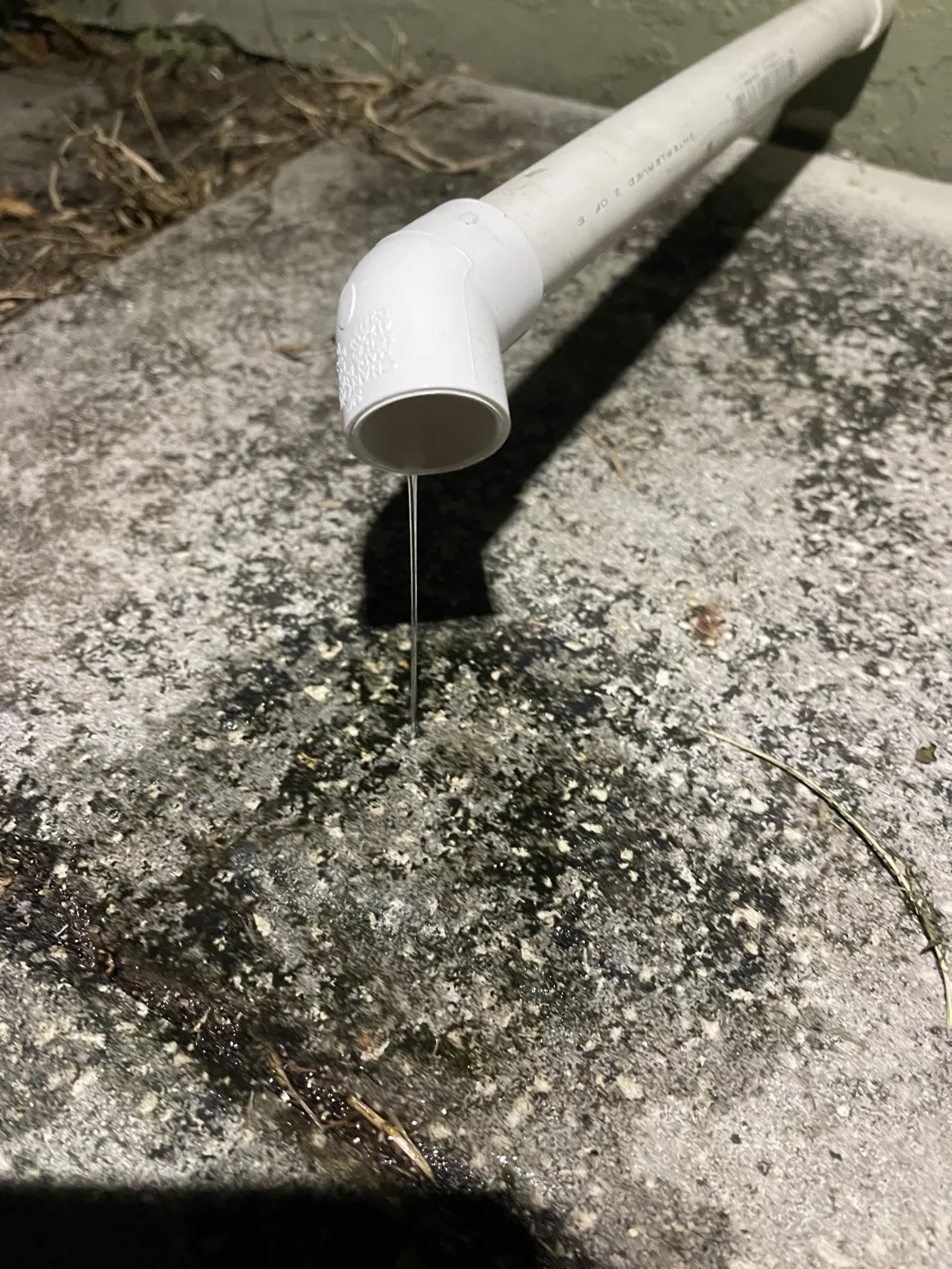 Water dripping from a condensate drain elbow onto a stained pad outside
