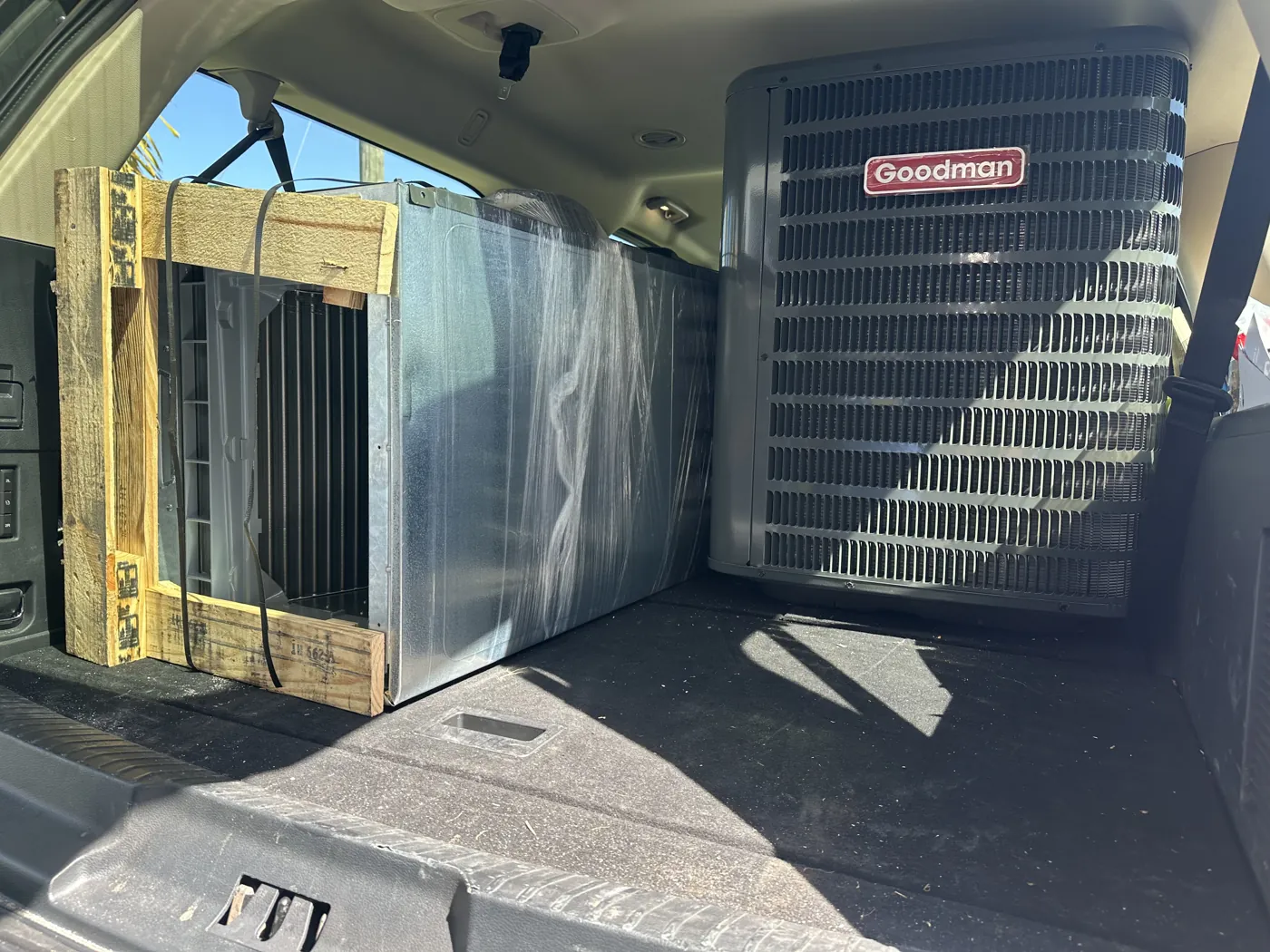A crated condenser and a plastic-wrapped air handler loaded in a vehicle for delivery to an installation