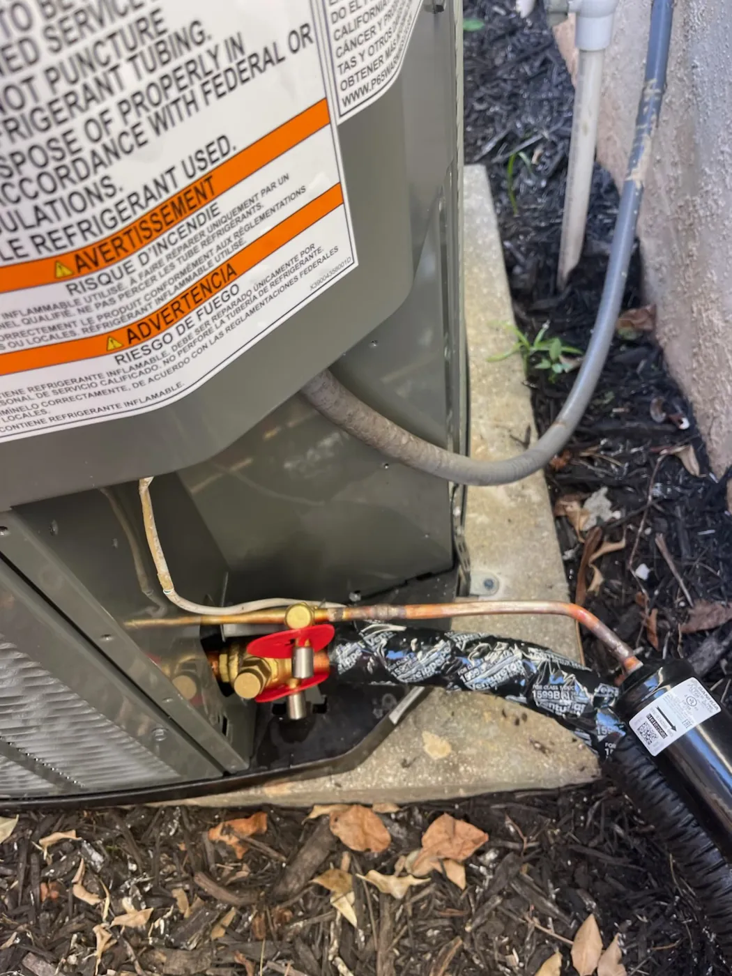 Insulated refrigerant lines meeting the service valves at the base of an outdoor unit, with the wrap sealed at the connection