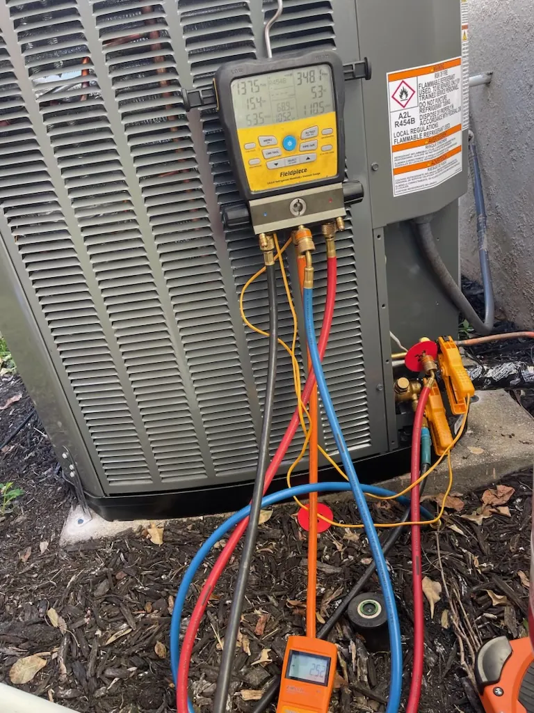 A digital manifold hanging on a condenser with test hoses connected during a diagnosis