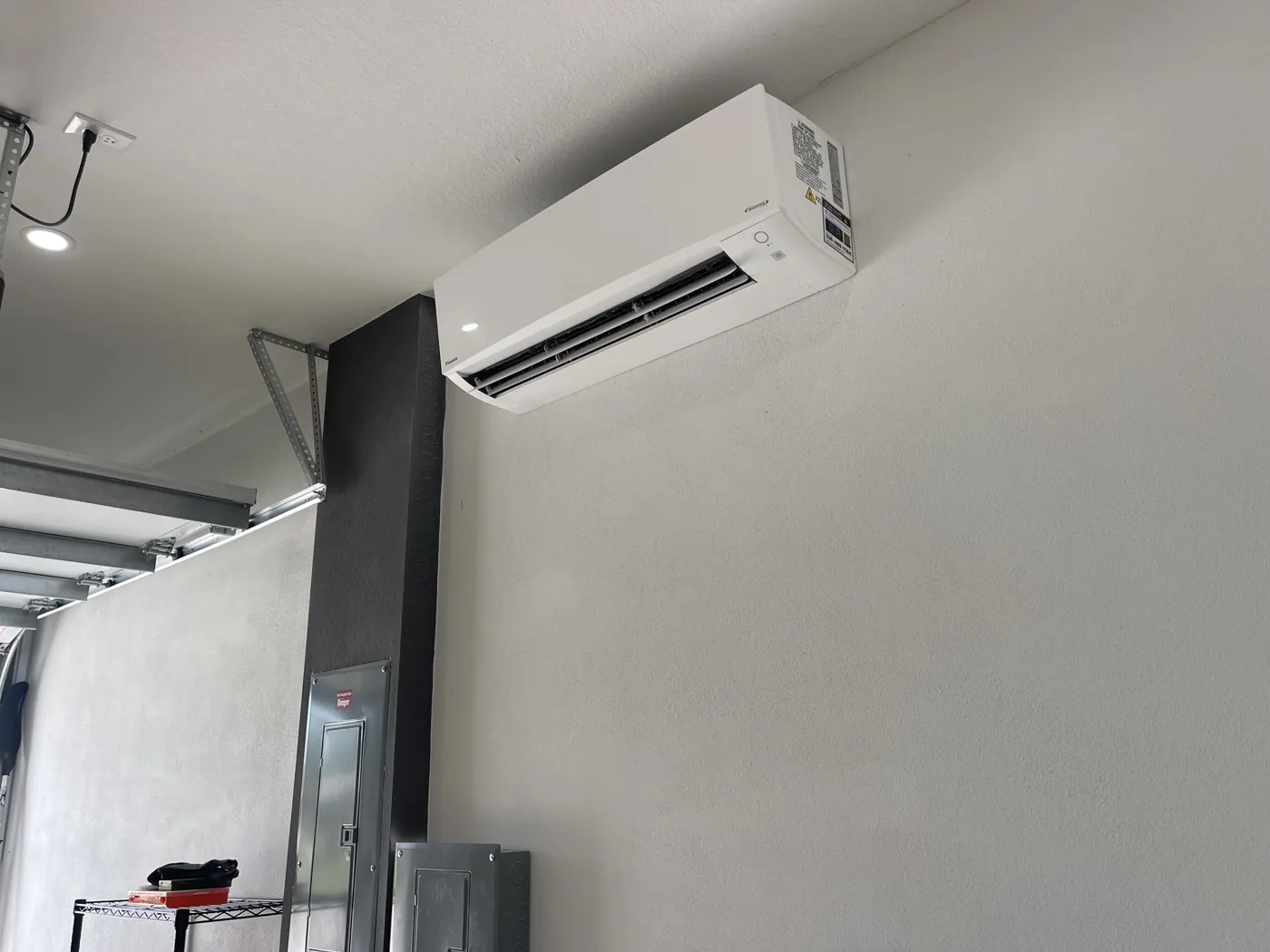 A mini-split indoor head mounted high in a garage corner, clearing the door track and hardware below
