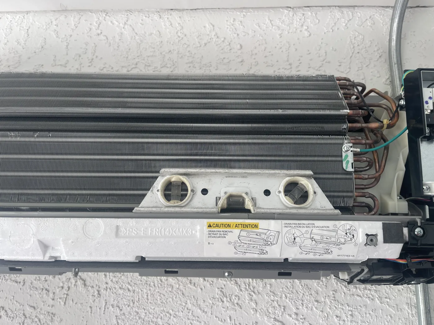 A mini-split head with the cover off, showing the coil face and the shallow tray that catches condensate