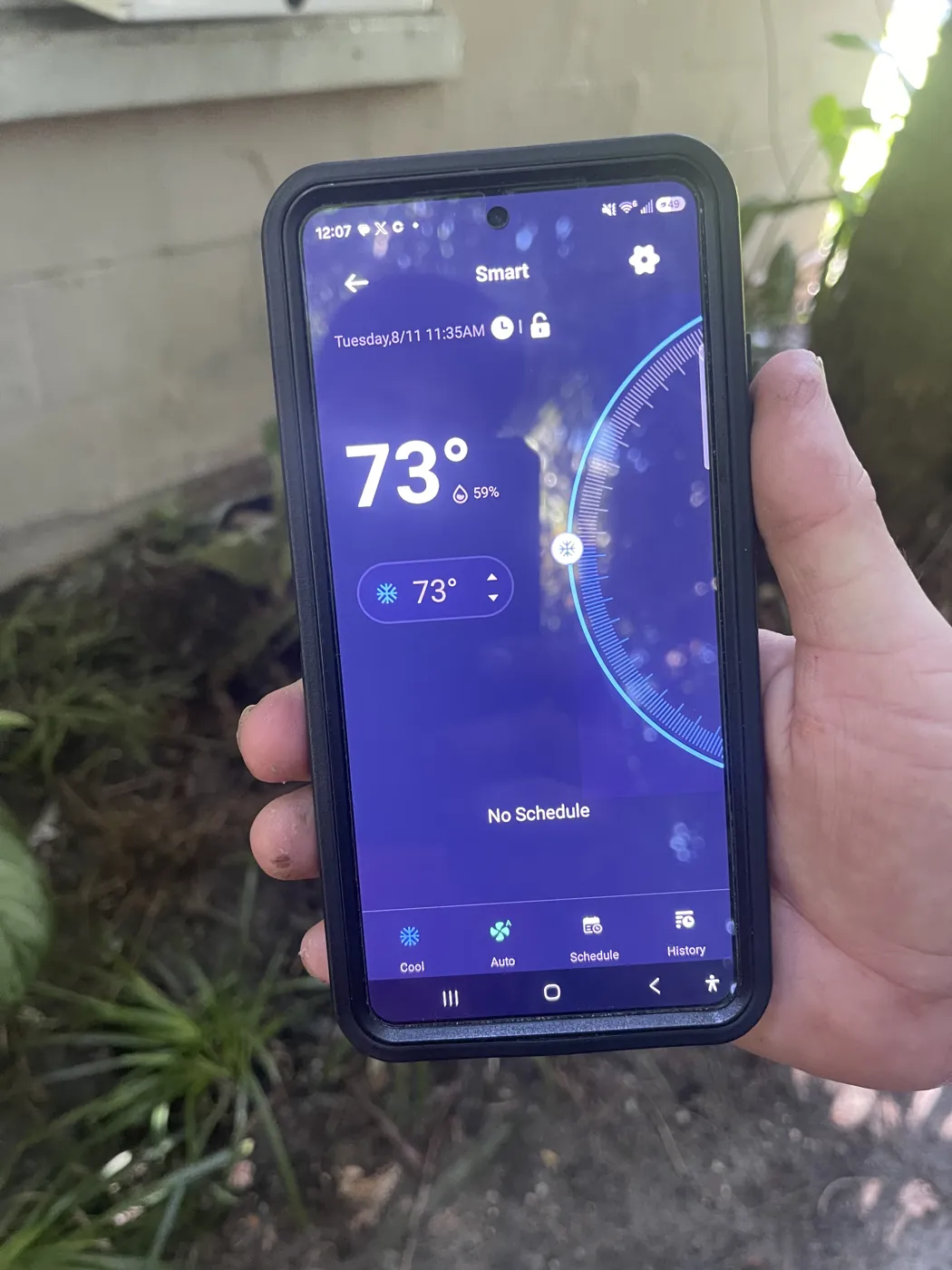 A hand holding a phone with a smart thermostat app showing 73 degrees and 59 percent indoor humidity