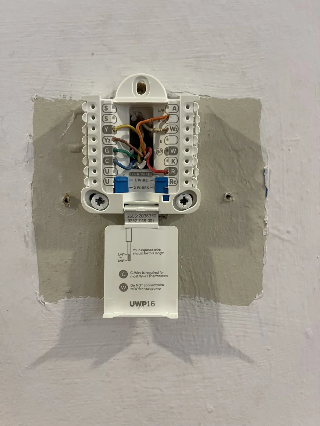 A thermostat pulled from its wall plate, exposing the labeled terminal base and low-voltage wires